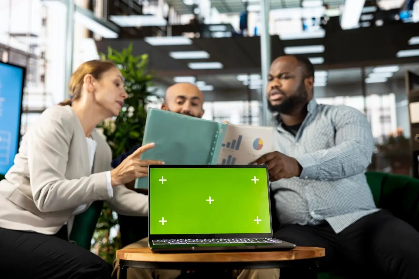 Ноутбук с хромакеем рядом с офисными сотрудниками, читающими статистику данных.